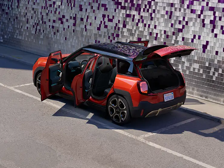 Rear top view of the all-electric MINI Aceman in Rebel Red and Black Roof with open doors on a street.